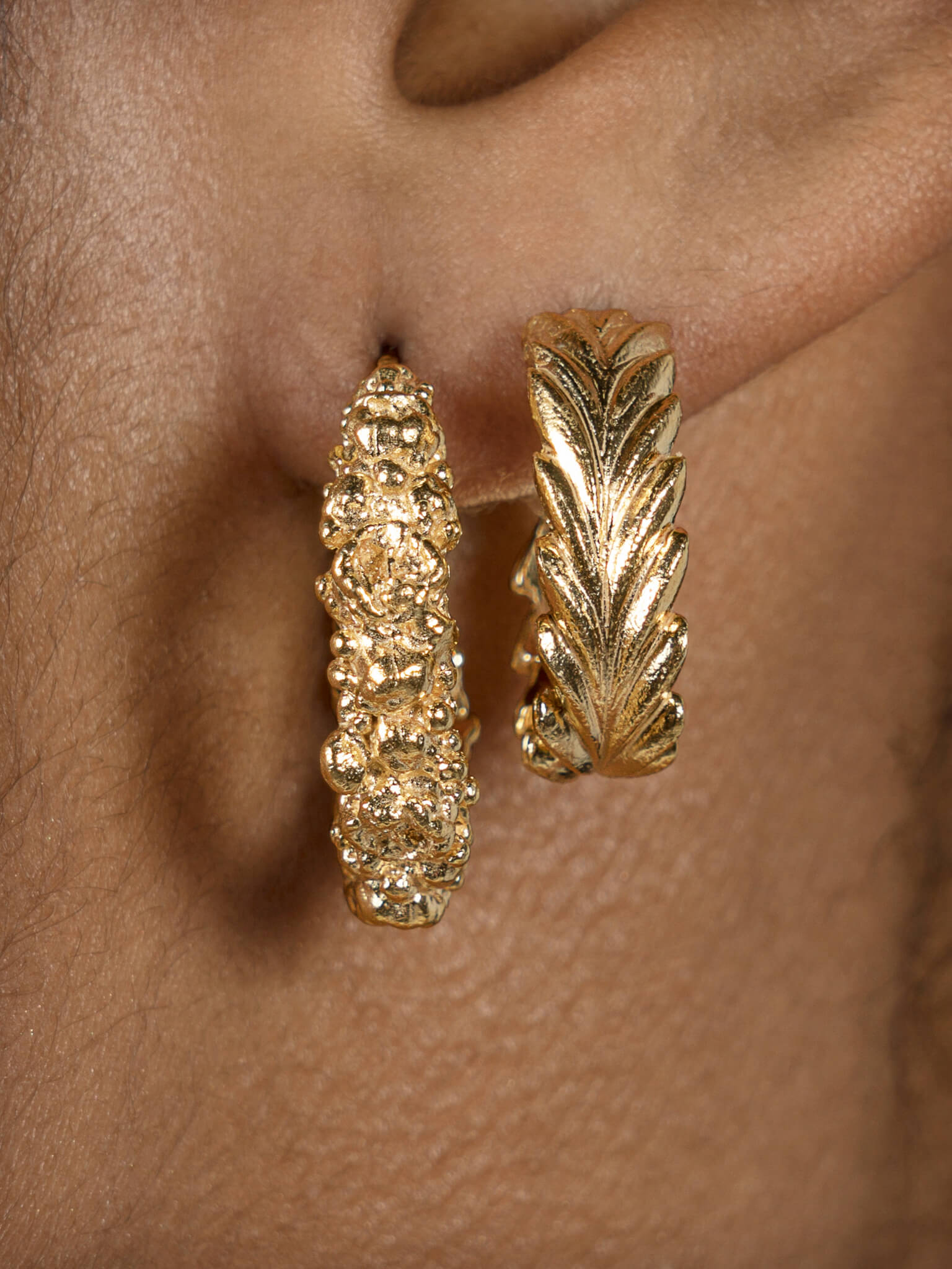 A close up of a woman's ear adorned with Cremilde Bispo Jewellery's Essential Leaf Hoops GP gold hoop earrings.