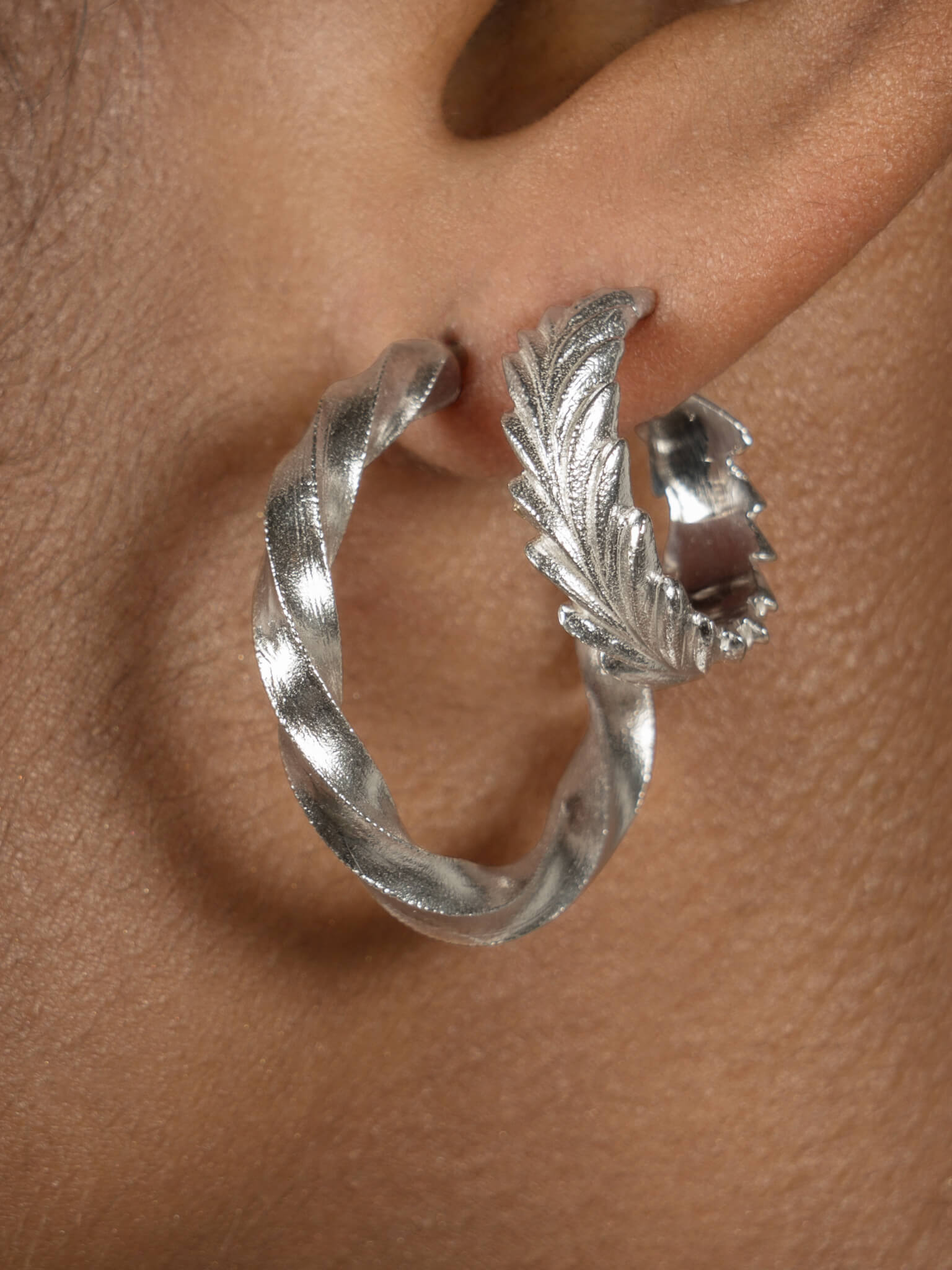 A close up of a woman's ear with a pair of Cremilde Bispo Jewellery Essential Leaf Hoops in silver, adding maximum style with minimal effort.
