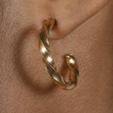 A close-up photo of a woman's hear featuring the Essential Twisted Hoops by Cremilde Bispo Jewellery in Gold Plated Silver.