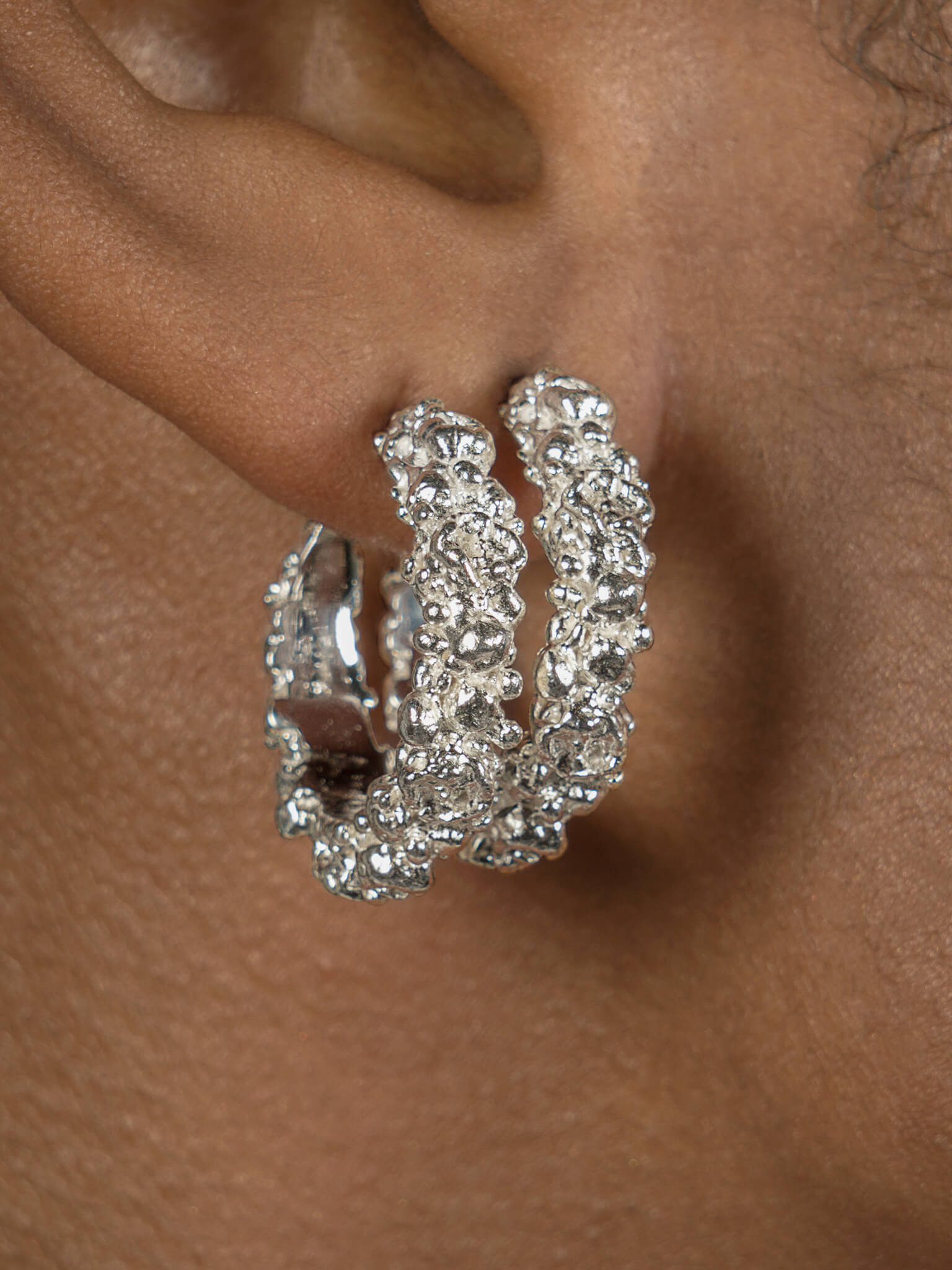 A close-up photo of a woman's hear featuring a pair of the Garden Hoops by Cremilde Bispo Jewellery in Sterling Silver.