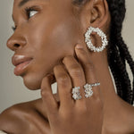 A black woman wearing a pair of handcrafted earrings adorned with floral foliage and The Garden Ring in sterling silver, embedded with Quartz, from Cremilde Bispo Jewellery.