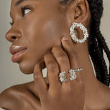 A black woman wearing a pair of handcrafted earrings adorned with floral foliage and The Garden Ring in sterling silver, embedded with Quartz, from Cremilde Bispo Jewellery.