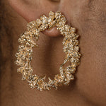 A woman's ear adorned with a Cremilde Bispo Jewellery Garden's Delight statement earrings, in gold plated sterling silver, with hand-sculpted nature inspired embellishments.