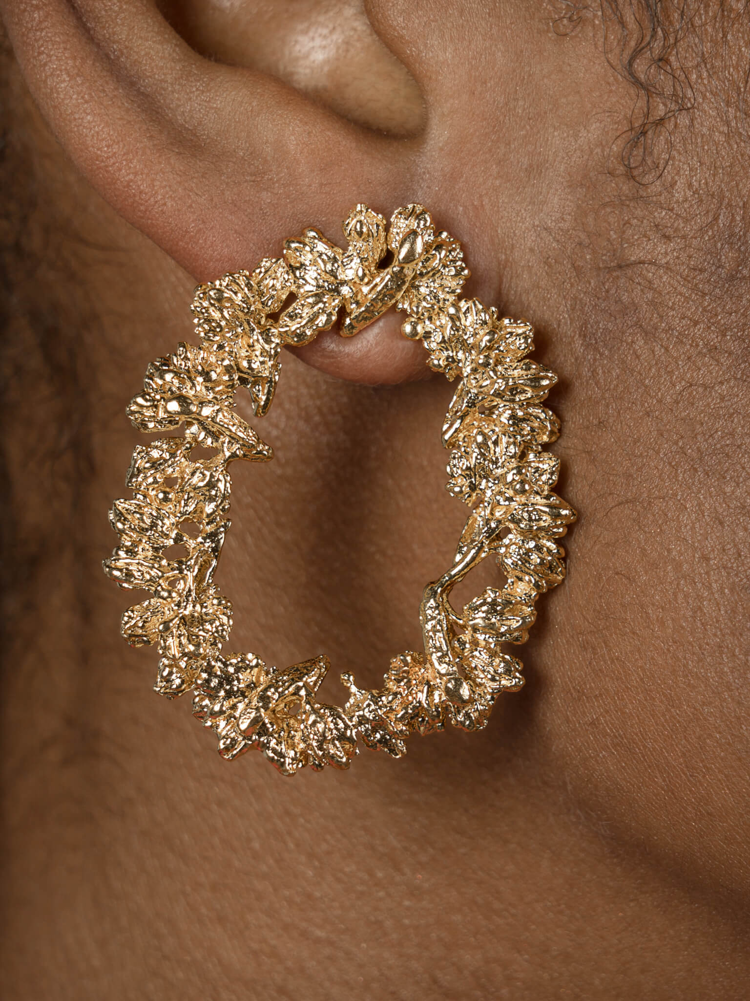 A woman's ear adorned with a Cremilde Bispo Jewellery Garden's Delight statement earrings, in gold plated sterling silver, with hand-sculpted nature inspired embellishments.