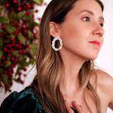 A refined woman is posing in front of a Christmas tree, showcasing the Cremilde Bispo Jewellery's Garden's Delight earrings, in sterling silver, which perfectly complement nature's beauty.
