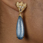 A woman's ear with a silver Cremilde Bispo Jewellery Muse III Kyanite earring, adorned with a blue teardrop, dangling from it.