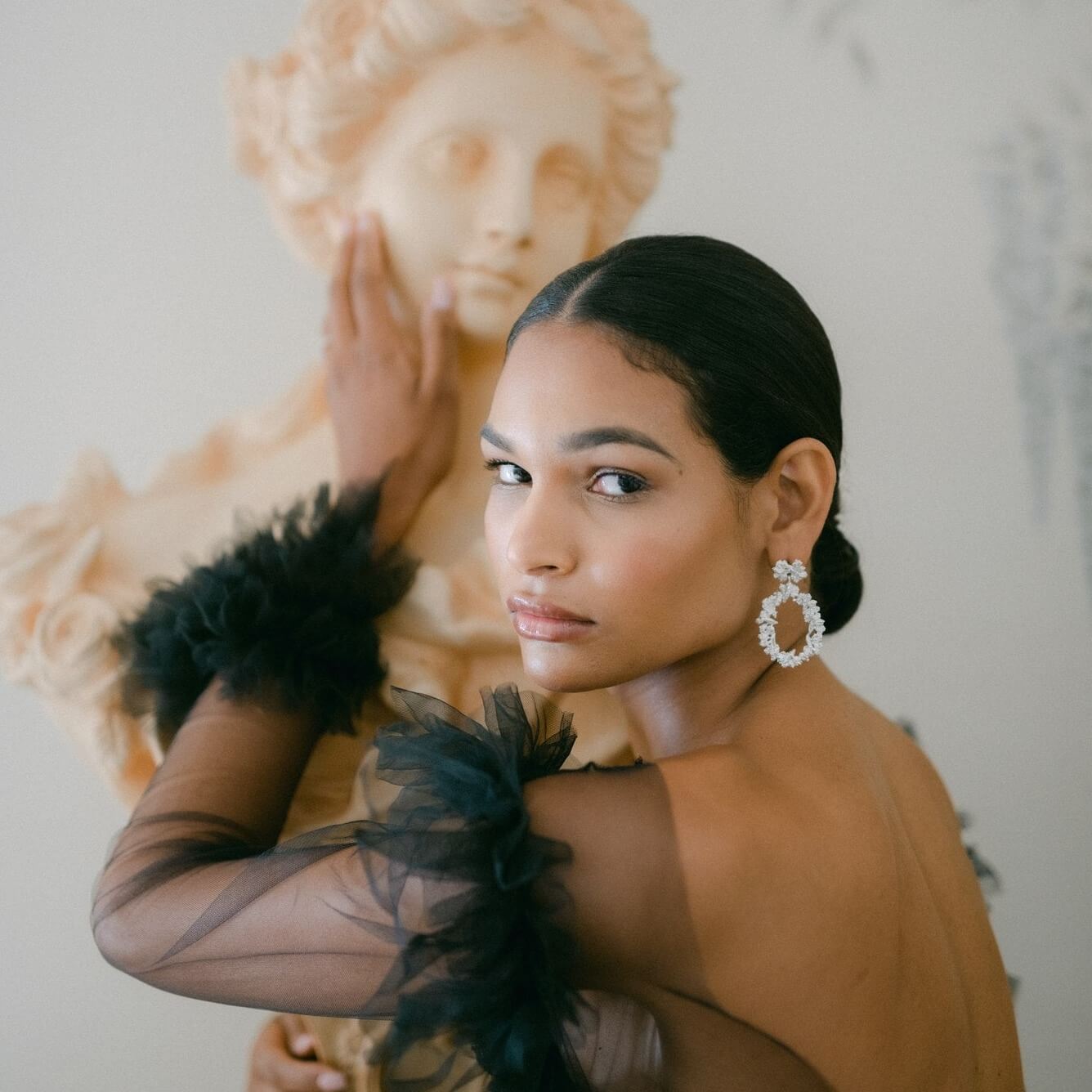 A sophisticated woman in a lavish black gown posing next to a statue adorned with the Garden's Delight statement earrings in sterling silver.