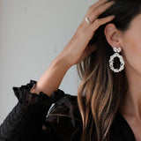 Close-up of a woman's ear elegantly adorned with the Cremilde Bispo Jewellery Garden's Delight statement earrings. Crafted from sterling silver, these earrings showcase intricate hand-sculpted floral details and a graceful, swaying drop-shaped design.