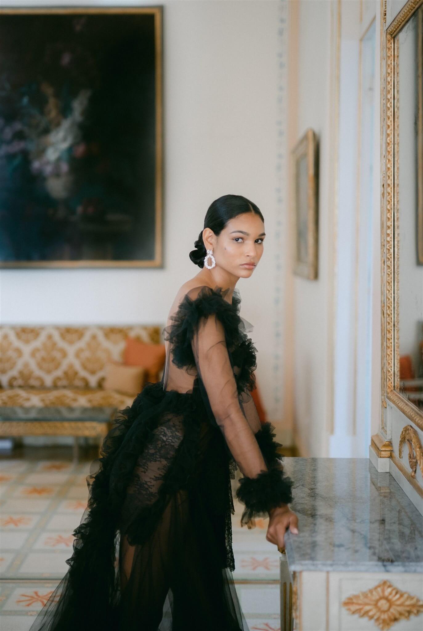 A sophisticated woman in a lavish black gown wearing the Cremilde Bispo Jewellery Garden's Delight statement earrings in sterling silver, posing in front of an luxury hotel mirror.