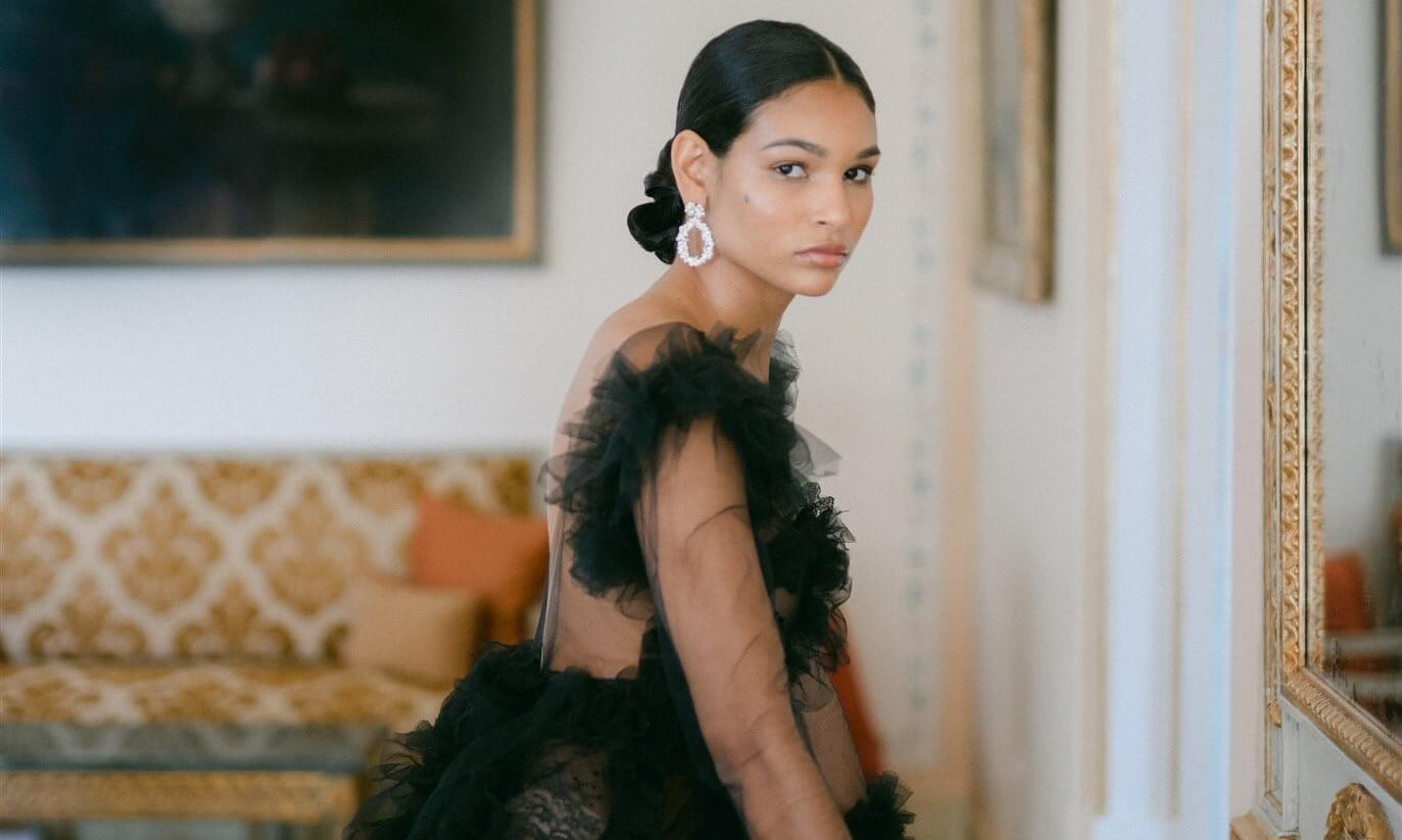 A sophisticated woman in a lavish black gown wearing the Cremilde Bispo Jewellery Garden's Delight statement earrings in sterling silver, posing in front of an luxury hotel mirror.