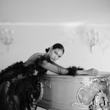 A black and white photo of a woman posing on a piano, showcasing opulence and wearing the Cremilde Bispo Jewellery earring set, The Garden's Delight II.