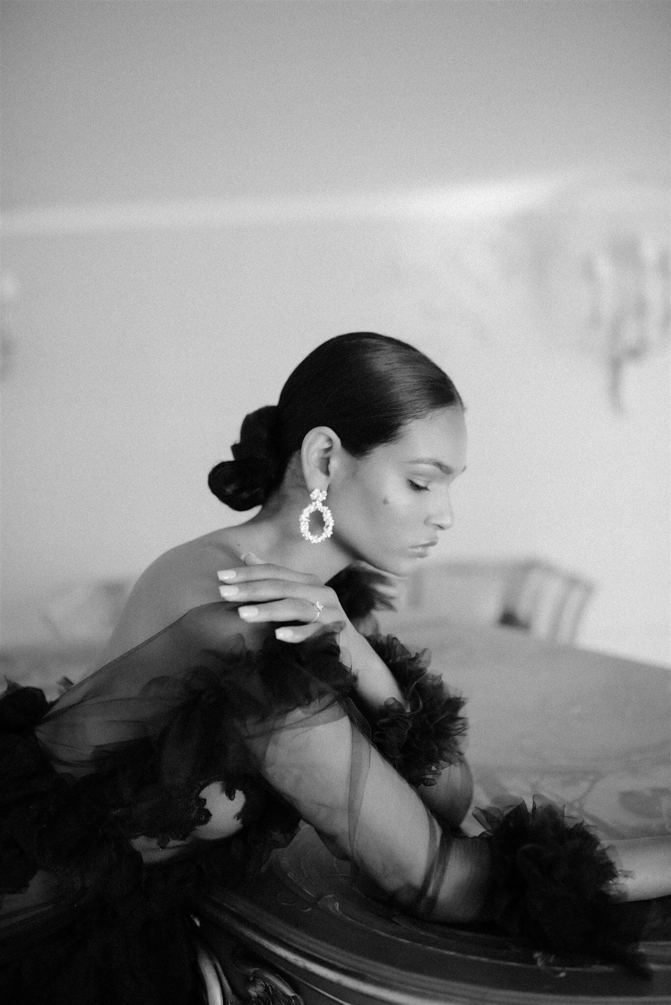 A sophisticated woman in a lavish black gown leaning on a grand piano wearing the Cremilde Bispo Jewellery Garden's Delight statement earrings in sterling silver.