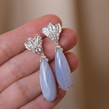 A hand holding a pair of The Muse III Chalcedony earrings, adorned with .925 silver accents by Cremilde Bispo Jewellery.