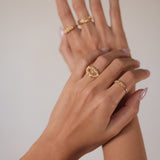 A woman's hand showcasing her jewellery collection with two elegant rings, including the exquisite Cremilde Bispo Jewellery 18K Yellow Gold Essential Dot Ring.