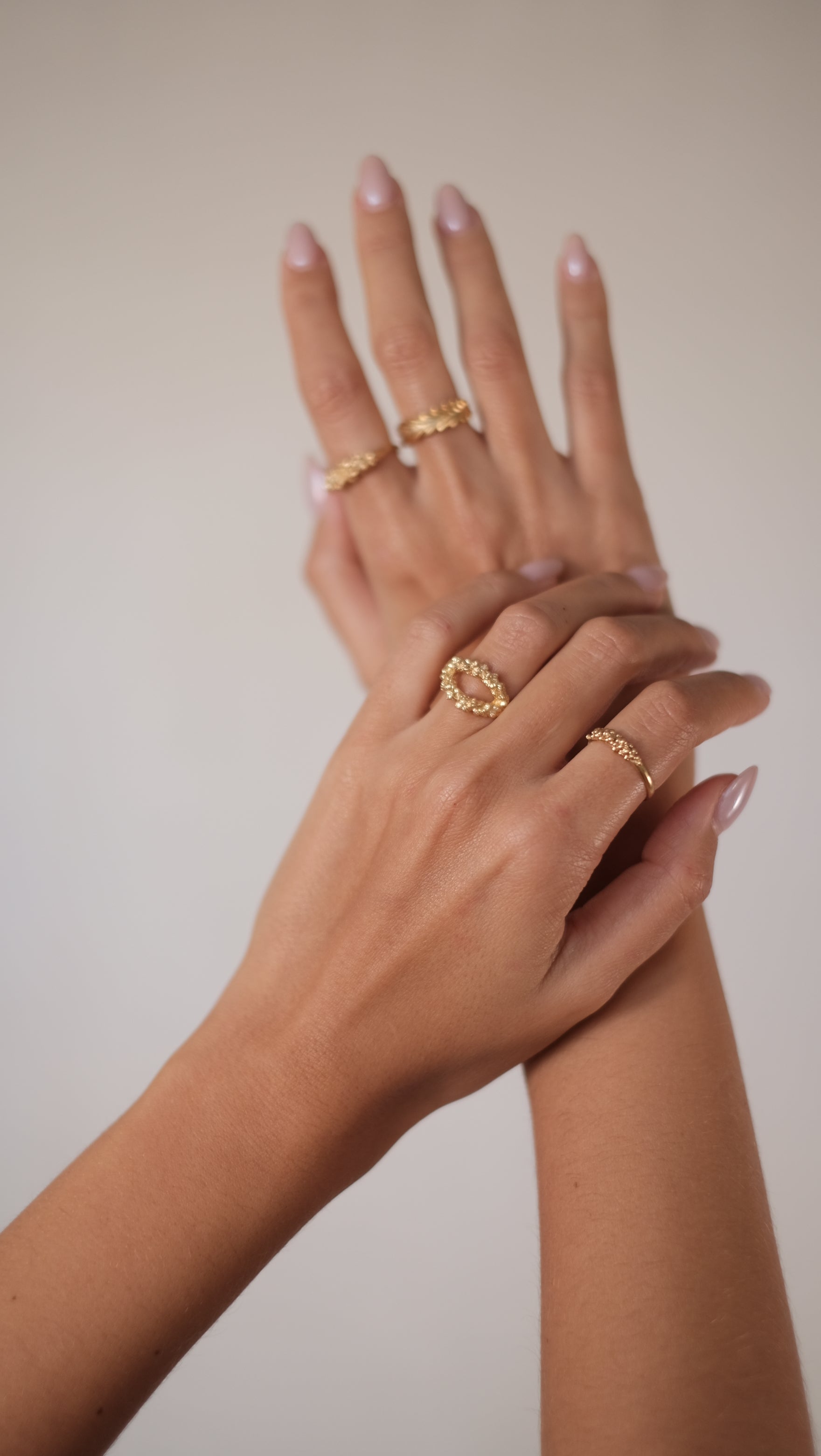 A woman's hand showcasing her jewellery collection with two elegant rings, including the exquisite Cremilde Bispo Jewellery 18K Yellow Gold Essential Dot Ring.