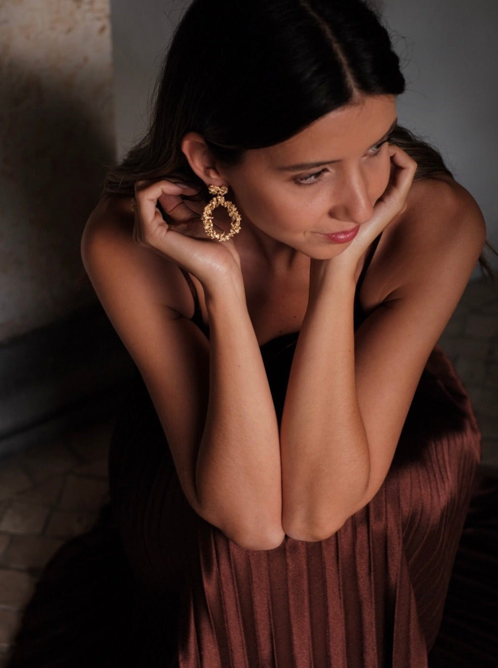 A woman exuding opulence in a brown dress with stunning gold earrings from the Cremilde Bispo Jewellery's Garden's Delight II GP earring set.