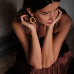 A woman exuding opulence in a brown dress with stunning gold earrings from the Cremilde Bispo Jewellery's Garden's Delight II GP earring set.