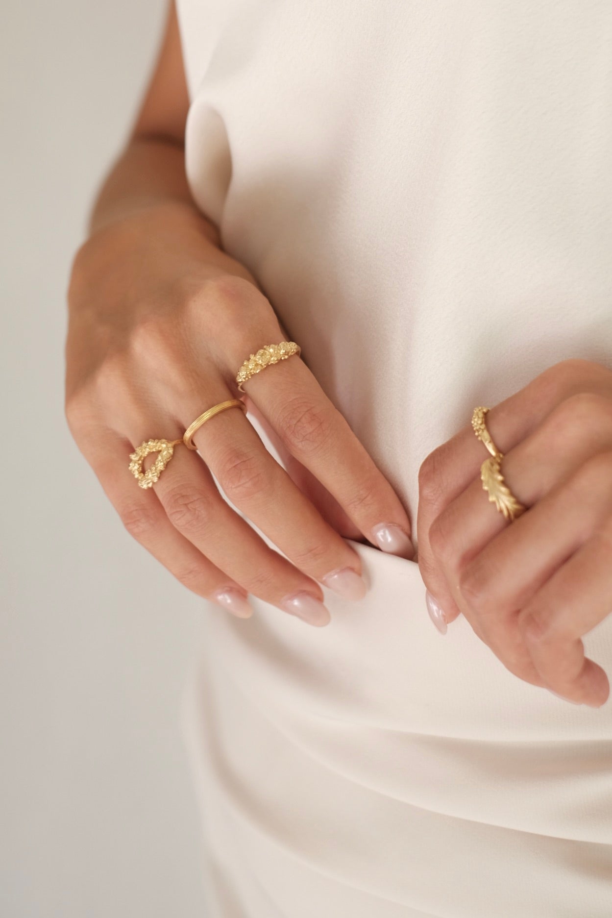 A woman adorned in an elegant white dress, complimented by exquisite Cremilde Bispo Jewellery's Laurel Ring GP inspired by Ancient Rome's grandeur. Each ring features meticulously hand-carved floral foliage designs reminiscent of the opulence.