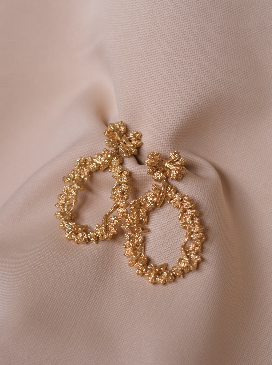 A pair of The Garden's Delight II GP hoop earrings by Cremilde Bispo Jewellery on a beige fabric.