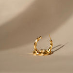 A fashionable woman's Essential Twisted Hoops GP earring by Cremilde Bispo Jewellery on a beige surface.