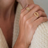 A woman wearing a white sweater and donning a Cremilde Bispo Jewellery Laurel Ring GP - a hand-carved floral foliage inspired by Ancient Rome's grandeur - accessorizes her ensemble.