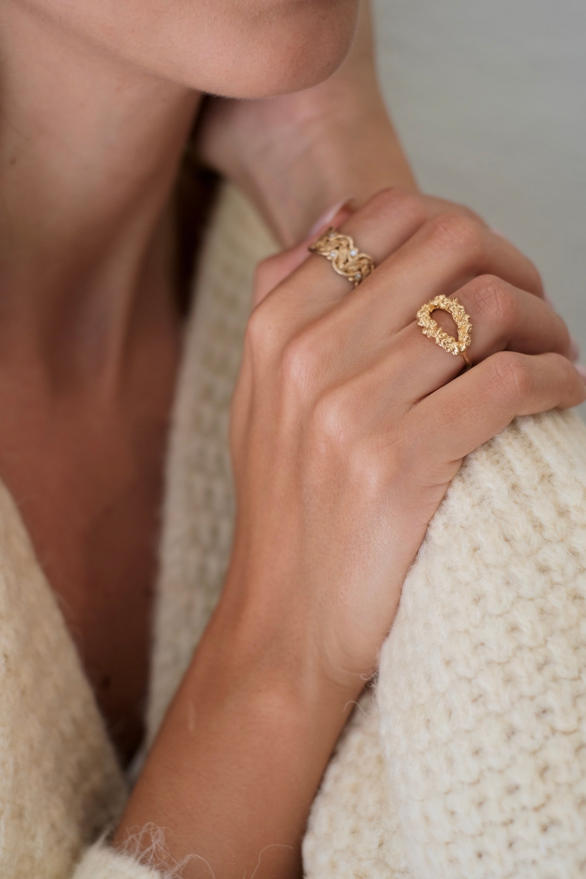 A woman wearing a white sweater and donning a Cremilde Bispo Jewellery Laurel Ring GP - a hand-carved floral foliage inspired by Ancient Rome's grandeur - accessorizes her ensemble.