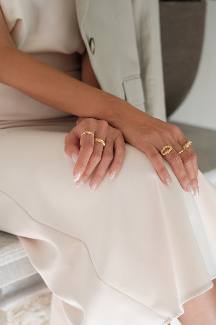 A woman, adorned with Cremilde Bispo Jewellery's hand-carved floral foliage gold rings, elegantly displays the timeless beauty of Ancient Rome's grandeur in her white dress. The Laurel Ring GP.