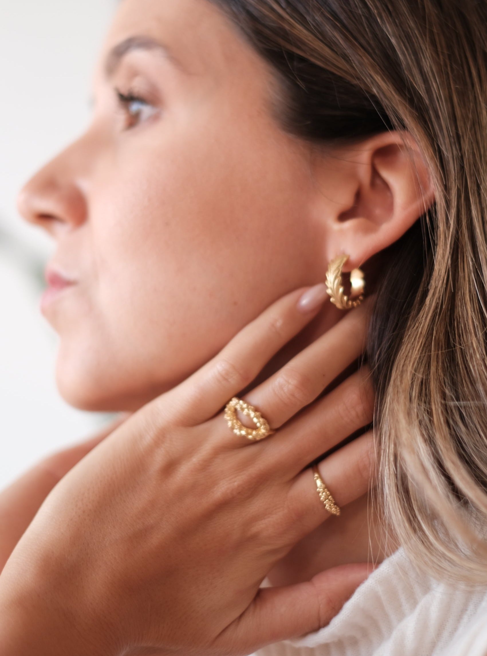 A woman exudes timeless elegance with her exquisite look, adorned with a Cremilde Bispo Jewellery Essential Dot Ring GP and earring.