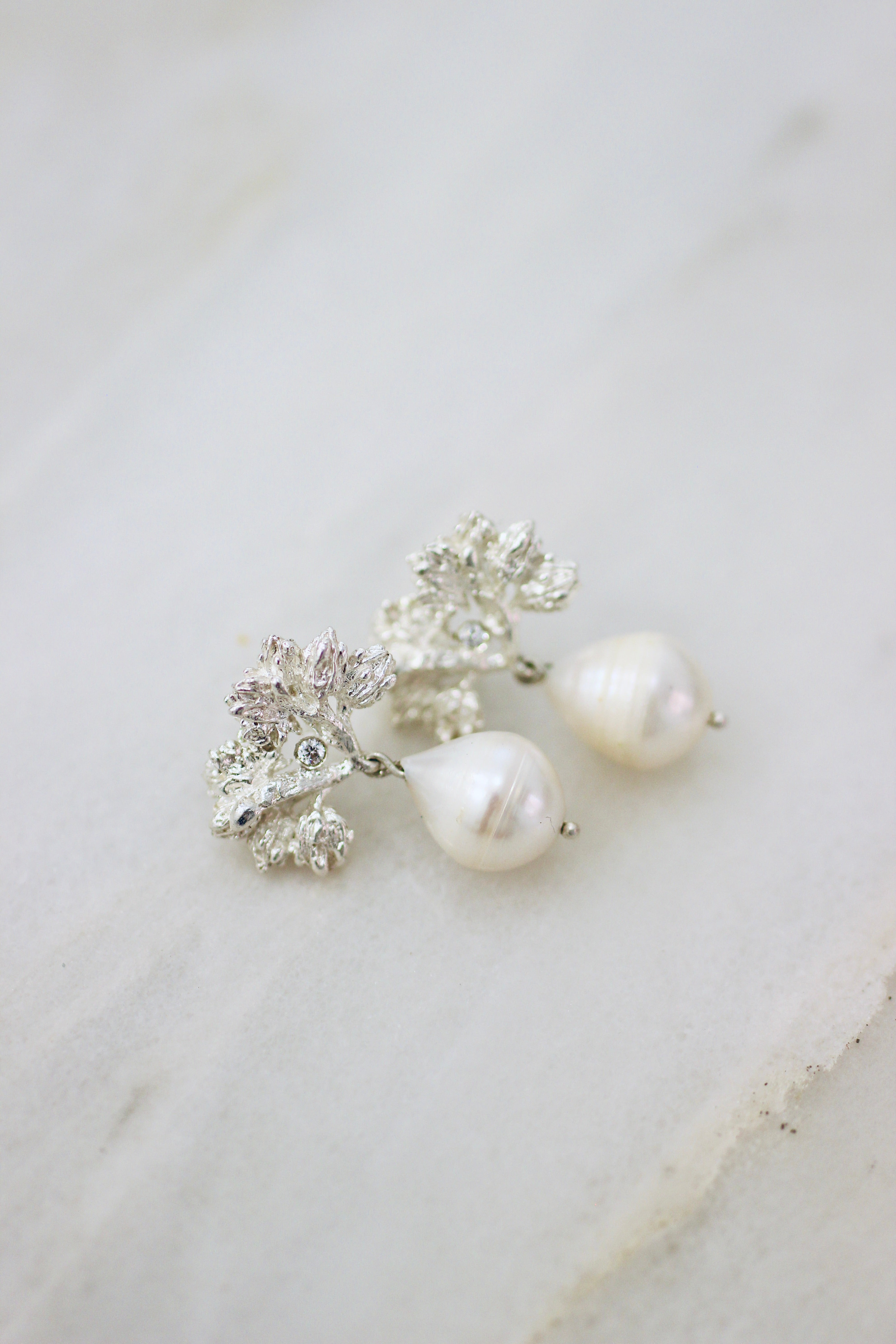 A pair of Cremilde Bispo Jewellery's Pearly Forest Earrings with Baroque Pearl accents on a marble surface.