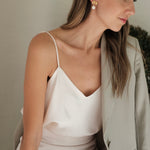 A woman in a white dress adorned with Cremilde Bispo Jewellery's Pearly Forest Earrings GP, sitting on a bench.