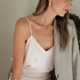 A woman in a white dress adorned with Cremilde Bispo Jewellery's Pearly Forest Earrings GP, sitting on a bench.