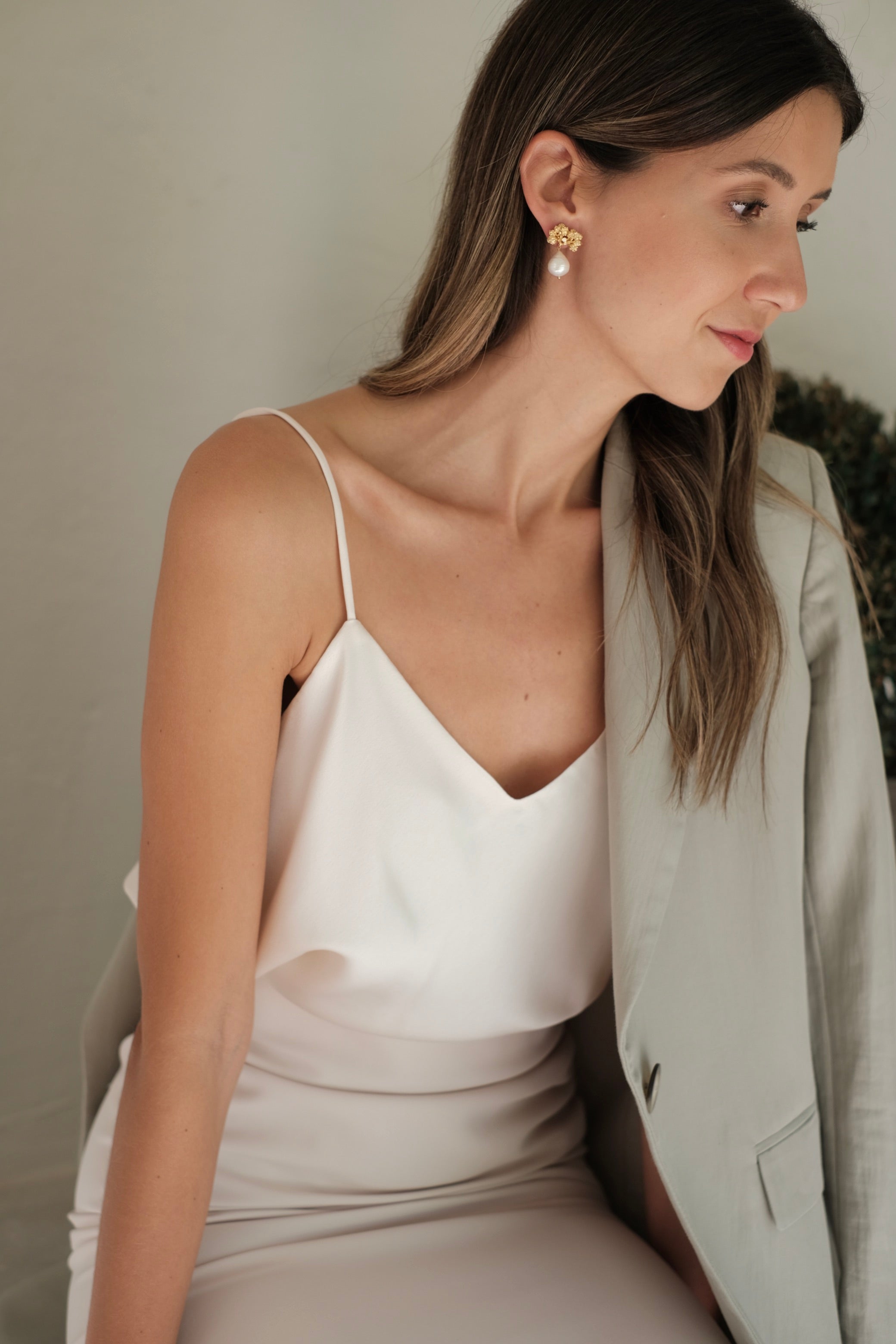 A woman in a white dress adorned with Cremilde Bispo Jewellery's Pearly Forest Earrings GP, sitting on a bench.